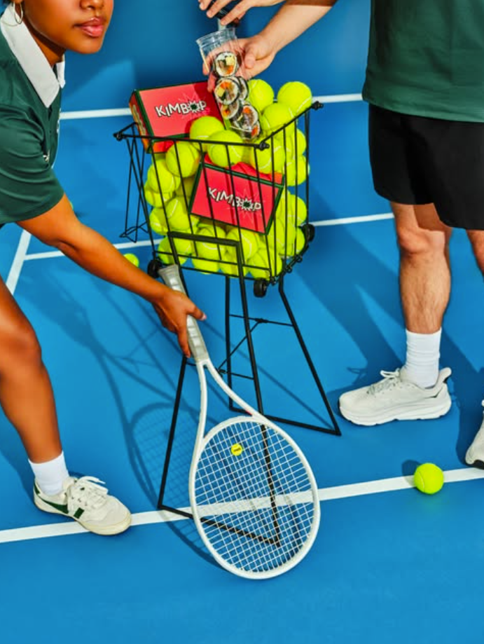 A tennis ball cart filled with tennis balls and red Dolldoll Kimbap boxes