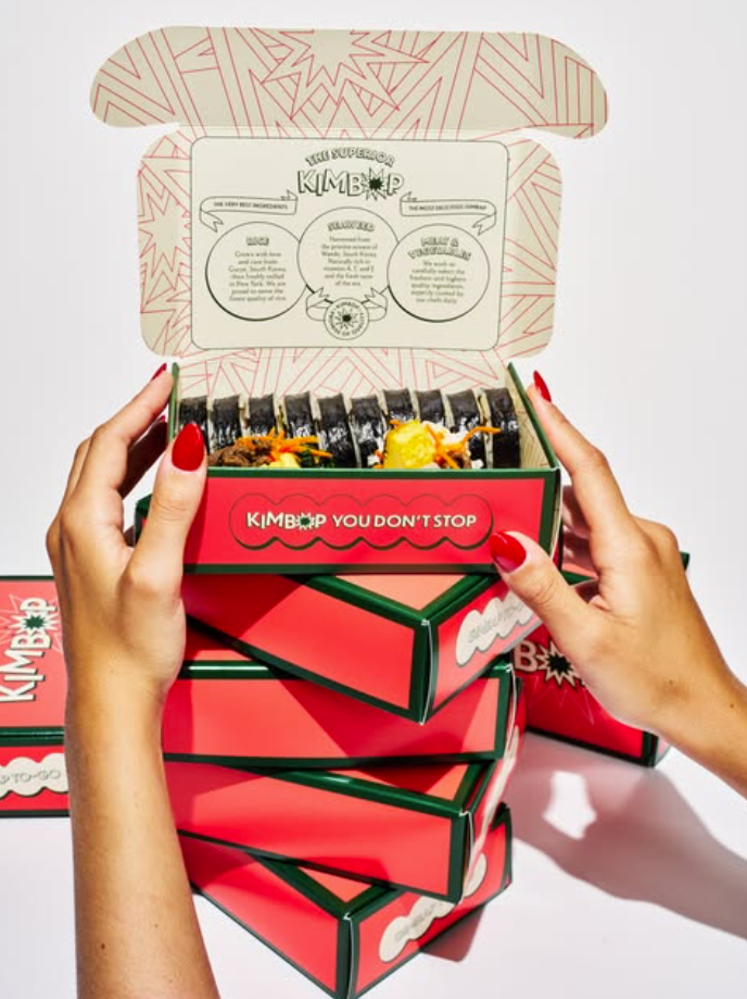 Hands opening a stack of red Dolldoll Kimbap boxes